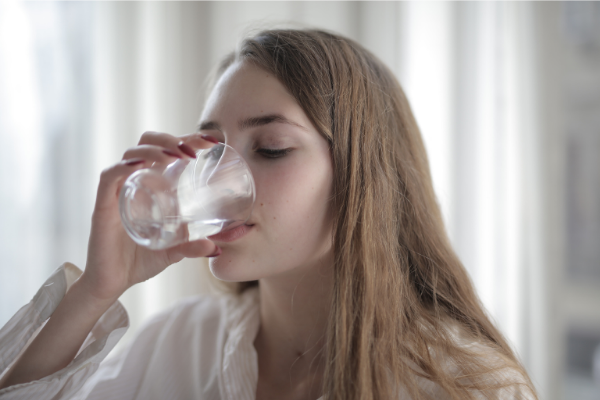 Eine blonde Frau trinkt mit geschlossenen Augen ein Glas Wasser.